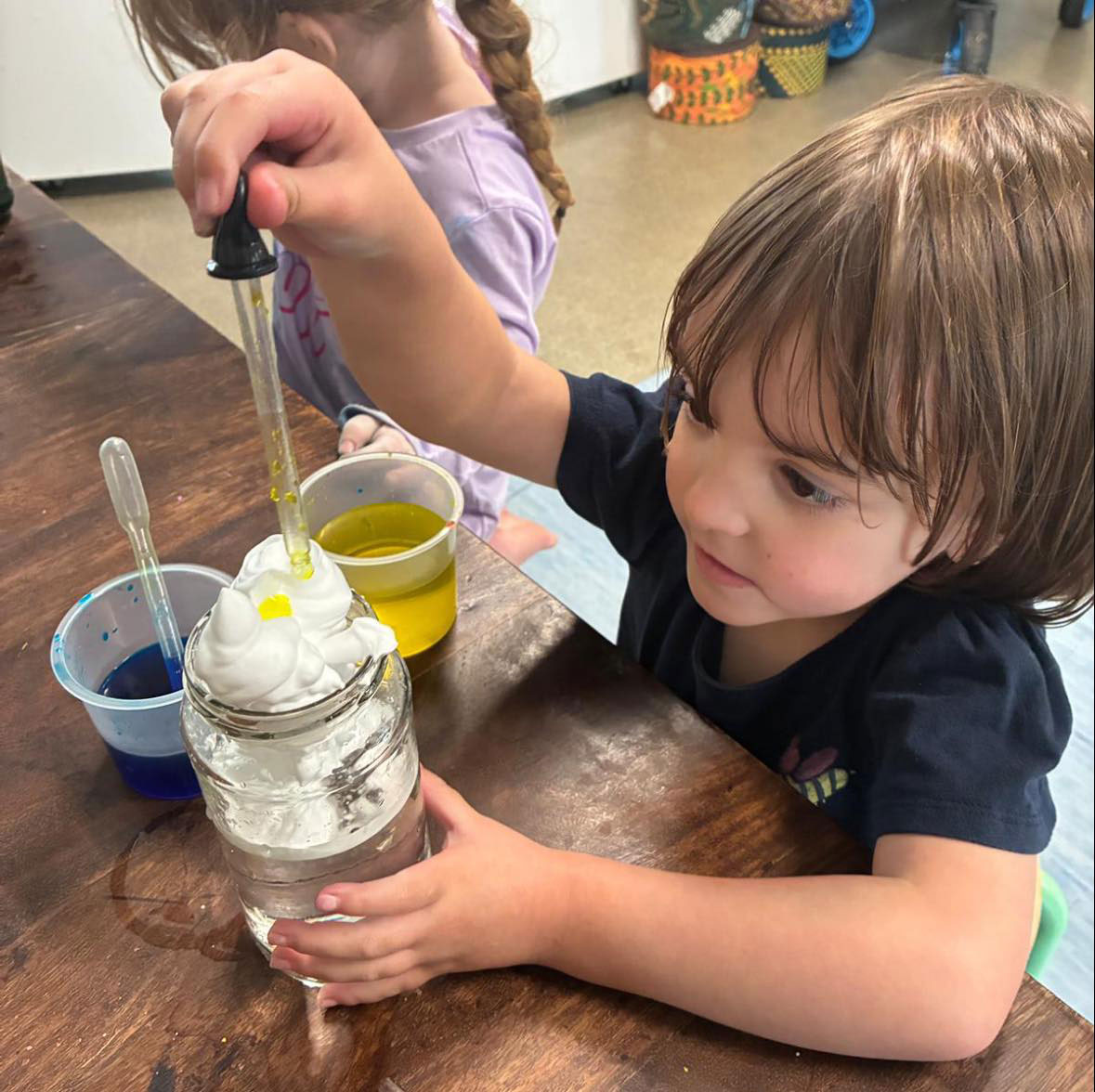 A photograph of a child playing with coloured liquids and foam in a jar